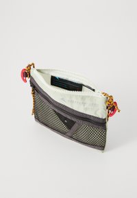 Bolsa con cremallera en gris y blanco con un lado de rejilla, cordón estampado y herrajes rojos. El interior cuenta con una etiqueta impresa y es texturizado.