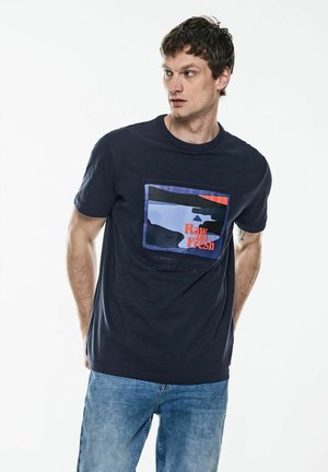 Námořnická modrá trička s kulatým výstřihem a obdélníkovou grafikou s odstíny modré a oranžové, na které je text "Raw and Fresh." Bavlněná tkanina.