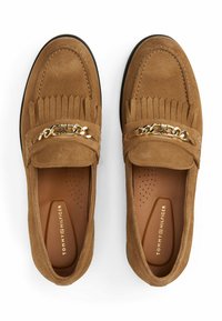 Brown suede loafers with fringe detailing and gold chain accent. Features a cushioned insole and a black rubber sole.