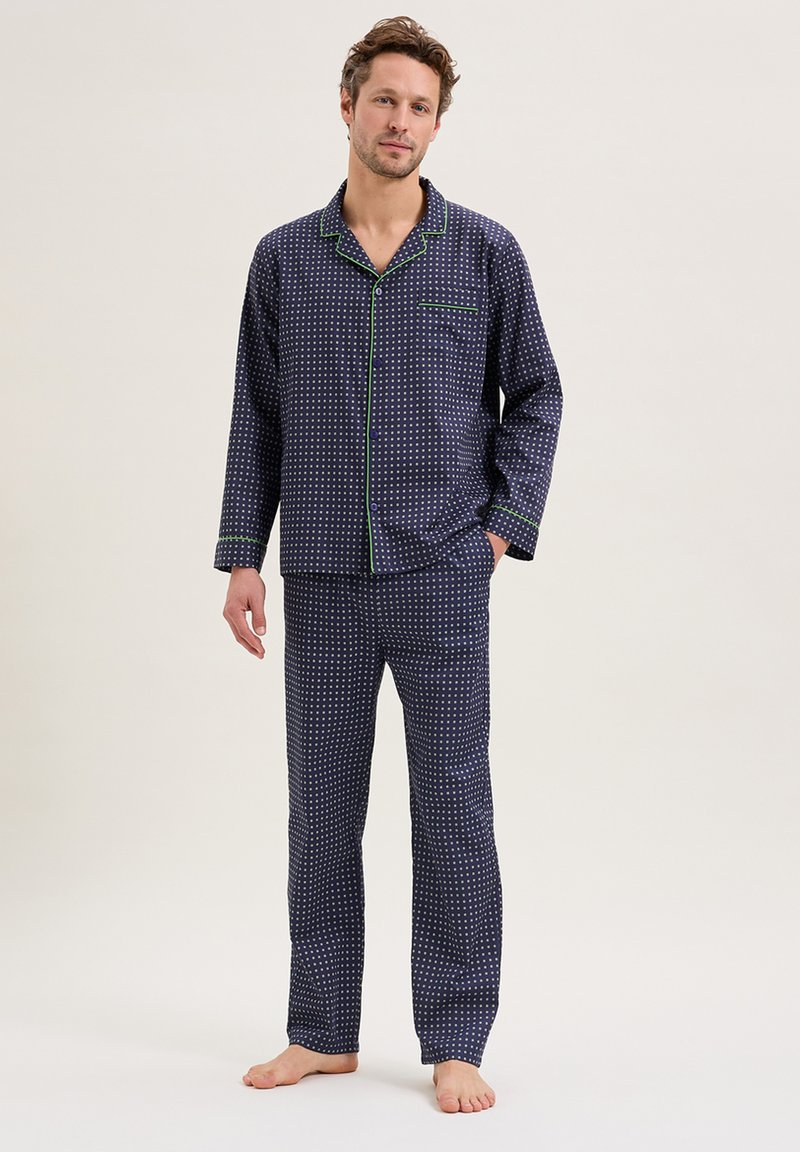 Ensemble de pyjama bleu marine avec des pois blancs, passepoil vert contrastant, manches longues, fermeture à boutons et pantalon à jambes droites. Matière en coton doux.