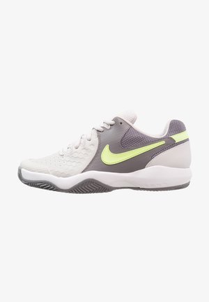 Witte en grijze sportschoen met honingraatstructuur, neongele Nike-swoosh, mesh enkelkraag en gestructureerde grijze zool.
