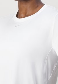 Camiseta deportiva blanca de Nike con cuello redondo, mangas cortas y una tela elegante y transpirable, con un logo discreto en el pecho.