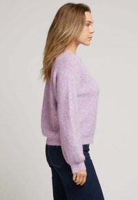 Pull en tricot violet clair avec une texture douce et duveteuse, des poignets côtelés et une coupe décontractée, associé à un jean en denim sombre.