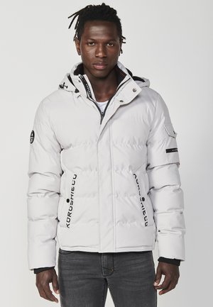 Giacca a vento bianca imbottita con cappuccio, dotata di accessori neri, dettagli con logo e tasche laterali con zip. Design testurizzato e trapuntato.