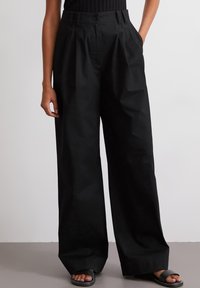 Zwarte wijde broek met een hoge taille, voorzien van een knoopsluiting aan de voorkant en zijzakken. Gemaakt van soepele, lichte stof met een matte afwerking.