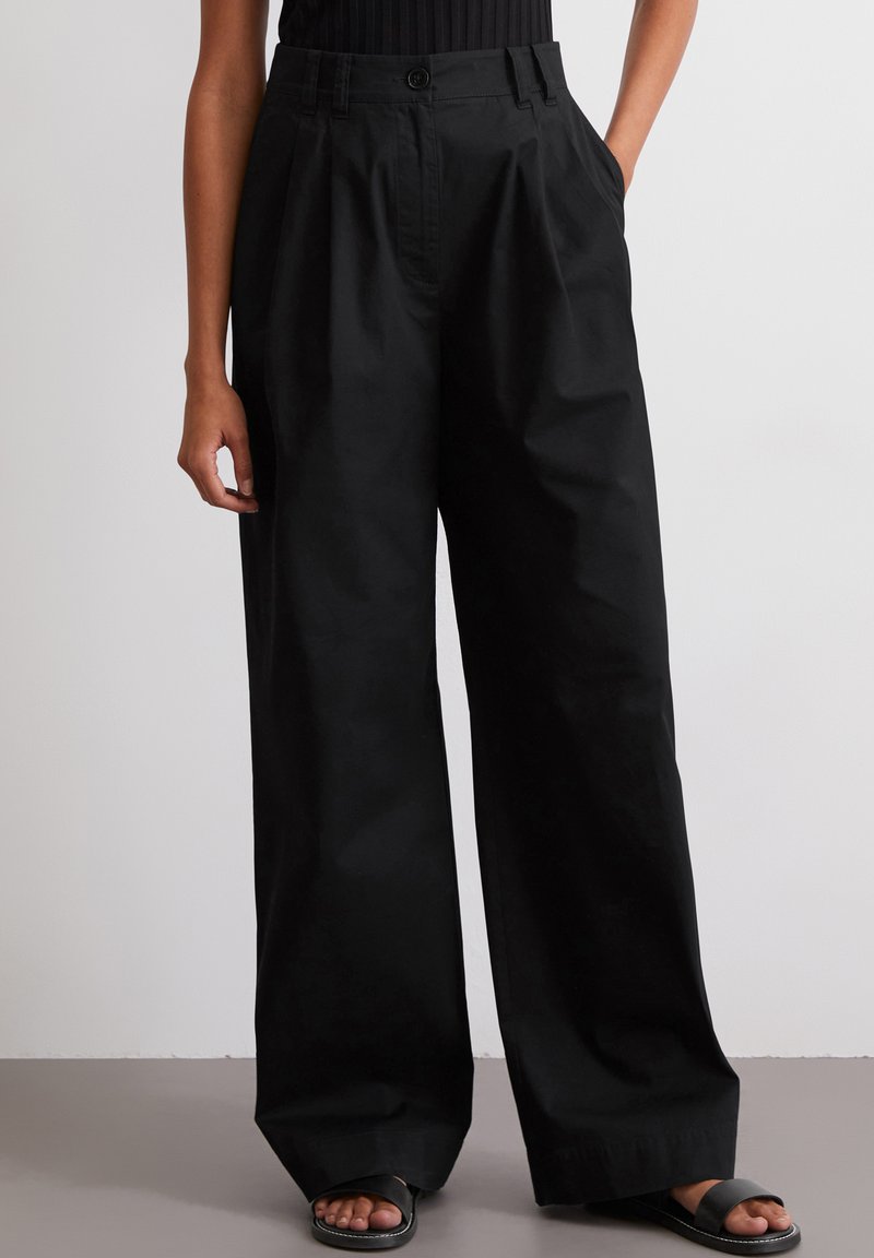 Zwarte wijde broek met een hoge taille, voorzien van een knoopsluiting aan de voorkant en zijzakken. Gemaakt van soepele, lichte stof met een matte afwerking.