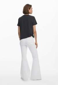 Black short-sleeve t-shirt paired with white flared jeans. The jeans have a frayed hem and a unique pocket design. Back view shown.