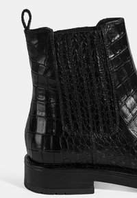 Bottines en cuir noir avec texture crocodile, panneaux latéraux élastiques et semelle plate. Équipées d'une languette à l'arrière pour un enfilage facile.