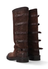 Hnědé semišové kozačky sahající ke kolenům s kulatou špičkou, vybavené pěti koženými pásky a přezkami po stranách. Silné, odolné podrážky.