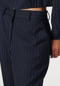 Pantaloni navy a righe con taglio su misura, dotati di una texture liscia, vita con passanti per cintura e tasche laterali.