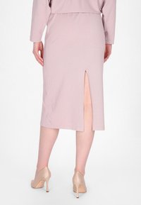 Lichtroze midi-rok van een textuurstof met een split aan de achterkant, gestructureerde taille en een zoom die net onder de knie valt.