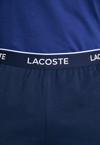 Marineblaue Lacoste-Shorts mit einer weichen Textur. Verfügt über ein Band mit "LACOSTE" in Weiß, akzentuiert von einem dünnen weißen Streifen über dem Bund.