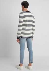 Neulepusero, jossa on vaakasuoria mustavalkoisia raitoja, pyöreä kaula-aukko, ribbireunat hihansuissa ja helmassa, yhdistettynä vaaleansinisiin farkkuihin ja valkoisiin tennareihin.