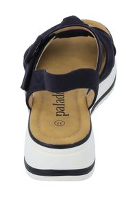 Sandalia azul marino con un diseño de cinta ancha, plantilla acolchada, suela de plataforma blanca y un acento negro alrededor de la base. Textura de tela suave.