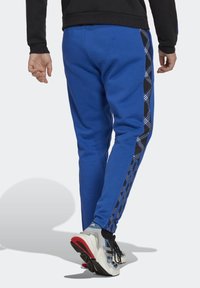 Blå sweatpants med en tapered fit, med en svart sidopanel dekorerad med ett geometriskt mönster. Bärs med ljusa träningsskor.