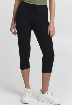 Svarta capri-joggingbyxor med elastisk midja och snörning, med upprullade anklar och sidofickor, i kombination med vita sneakers.
