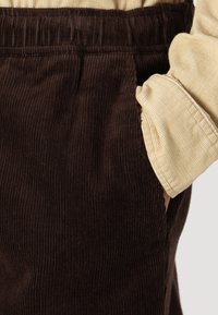 Bruna kordbyxor med ribbad textur, med en elastisk midja och sidofickor, i kombination med en ljusbeige ärm med uppvikt kant.