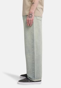 Ανοιχτό μπλε, ευρύχωρο τζιν από denim με ξεθωριασμένο φινίρισμα, διαθέτει ίσια κοπή και λεπτομερείς ραφές. Συνδυάζεται με μαύρα παπούτσια.