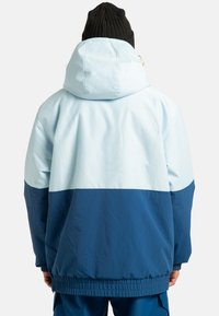 Jasnoniebieska i granatowa kurtka przeciwwiatrowa z kapturem, elastycznymi mankietami i ściąganym dołem; posiada wzór w blokach kolorów oraz gładką teksturę.