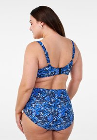 Modra bikini z cvetličnim vzorcem s širokimi naramnicami in visokim pasom. Material deluje gladko z rahlim sijajem. Odtisi za zapiranje na hrbtu so opazni.