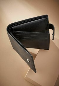 Portefeuille en cuir noir avec une texture granuleuse, des compartiments pour cartes et une fermeture à pression, présenté ouvert sur un fond neutre.