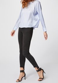 Blusa a righe azzurro chiaro con maniche lunghe, abbinata a jeans skinny neri. L'outfit presenta tacchi a stiletto neri con dettagli borchiati.