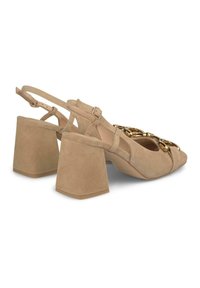 Sandales à talons en daim beige avec une ouverture à l'avant, un talon bloc, une bride réglable et un détail en chaîne décoratif sur le devant.