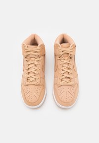 Par beige højtop-sneakers i lysebrun med perforerede tåbokse, snørebånd og Velcro-stropper, vist oppefra på en hvid baggrund.