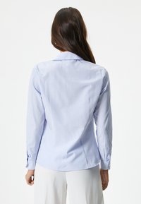 Camicia a maniche lunghe azzurro chiaro con righe bianche verticali, dotata di colletto classico e polsini con bottoni, realizzata in tessuto a trama liscia.