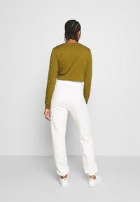 Olivově zelené tričko s dlouhým rukávem spárované s bílými tepláky na gumu. Bílé tenisky dotvářejí ležérní outfit. Jednoduchý design a pohodlný střih.