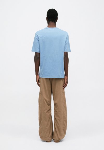 Ανοιχτό μπλε βαμβακερό μπλουζάκι με κανονικό λαιμό, συνδυασμένο με χαλαρές μπεζ βαμβακερές παντελόνες, που παρουσιάζουν μια χαλαρή σιλουέτα.