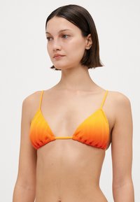 Trekantet bikini topp i gradient oransje. Teksturert stoff med tynne justerbare stropper og en midtforbinder. Ingen merkbar maskinvare eller mønstre.