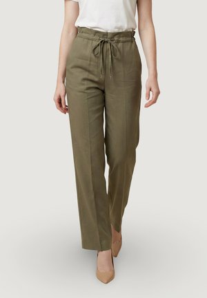 Donna che indossa pantaloni a gamba larga olive a vita alta con coulisse e tacchi beige a punta, abbinati a una maglietta bianca a maniche corte.