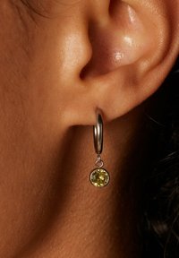 Silberner Creolenohrring mit einem runden, gelben Edelsteinanhänger. Die Creole ist poliert und der Edelstein hat Facetten, die einen funkelnden Effekt erzeugen.