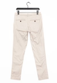 Pantalons en coton beige suspendus à un cintre noir, présentant deux poches arrière avec des boutons marron et un design à jambe droite.