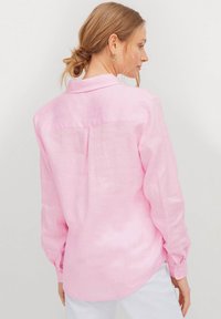 Camicia di lino rosa con yoke sul retro, maniche lunghe e polsi con bottoni. Presenta una vestibilità rilassata e una texture liscia.