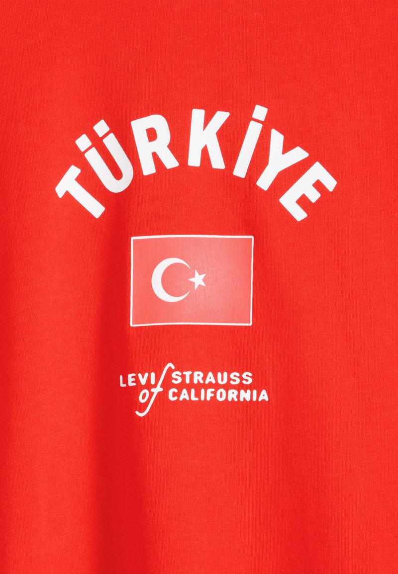 Red fabric with white text "TÜRKİYE" above a white-outlined Turkish flag and "Levi Strauss of California" below.