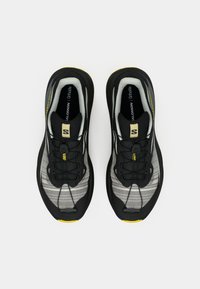 Τα ανδρικά αθλητικά παπούτσια σε μαύρο και γκρι έχουν πλεκτό επάνω μέρος, σύστημα γρήγορου δέσιμου και κίτρινη λεπτομέρεια στη σόλα. Ο σχεδιασμός περιλαμβάνει υφή με σχέδιο.