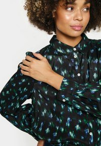 Camisa negra de botones con un patrón multitonal en verde y azul. Hecha de tela suave con mangas largas y cuello clásico.