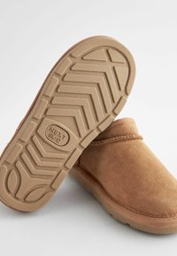 Scarpe slip-on in suede color tan con suole in gomma, caratterizzate da un motivo di grip testurizzato e dettagli cuciti lungo il bordo. Marchio sulla suola.