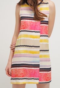 Ärmlös klänning med flerfärgade horisontella ränder i rosa, gult och svart. Tillverkad av lättviktsmaterial med en jämn yta.