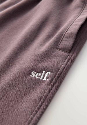 Lágy anyagból készült lila melegítőnadrág, oldalsó zsebből és a szegély közelében elhelyezkedő fehér hímzett "self." logóból áll.