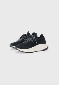 Black knit sneakers with textured upper, white midsole, and black rubber outsole. Black and white patterned laces and branded accents visible.
