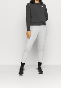 Zwarte sweatshirt met lange mouwen en ronde hals, gecombineerd met grijze leggings. Schoenen: zwarte sportschoenen. Glad materiaal, aansluitend ontwerp, minimale branding.