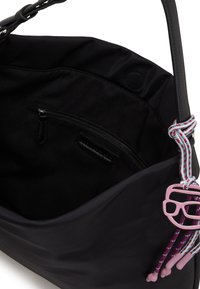 Black tote bag with a soft fabric interior, zip pocket, and a pink sunglasses charm attached to braided cord. Features a structured shape.