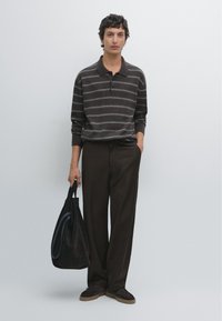 Polo a maniche lunghe a righe marroni, pantaloni larghi marroni scuri e una borsa a tracolla nera in tessuto. Scarpe scamosciate con suola in gomma.