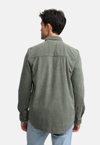 Camisa de pana verde con cuello, puños abotonados y textura acanalada vertical. Diseñada con un corte recto y detalle de yugo en los hombros.