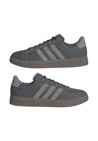 Un paio di sneakers Adidas grigie con tre strisce grigie più chiare, design con lacci e suole marroni, mostrati da viste laterali.