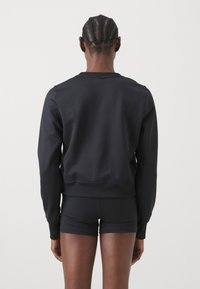 Zwarte sweatshirt met een ronde hals, lange mouwen en een getailleerde pasvorm. Gemaakt van een gladde stof, met ribboorden aan de mouwen en onderkant.