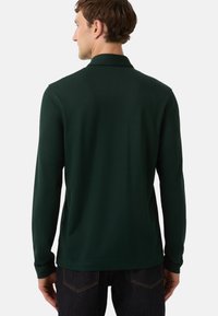 Dunkelgrünes, langärmeliges Poloshirt mit Kragen, glattem Stoff und figurbetontem Schnitt, kombiniert mit dunklen Denim-Jeans.